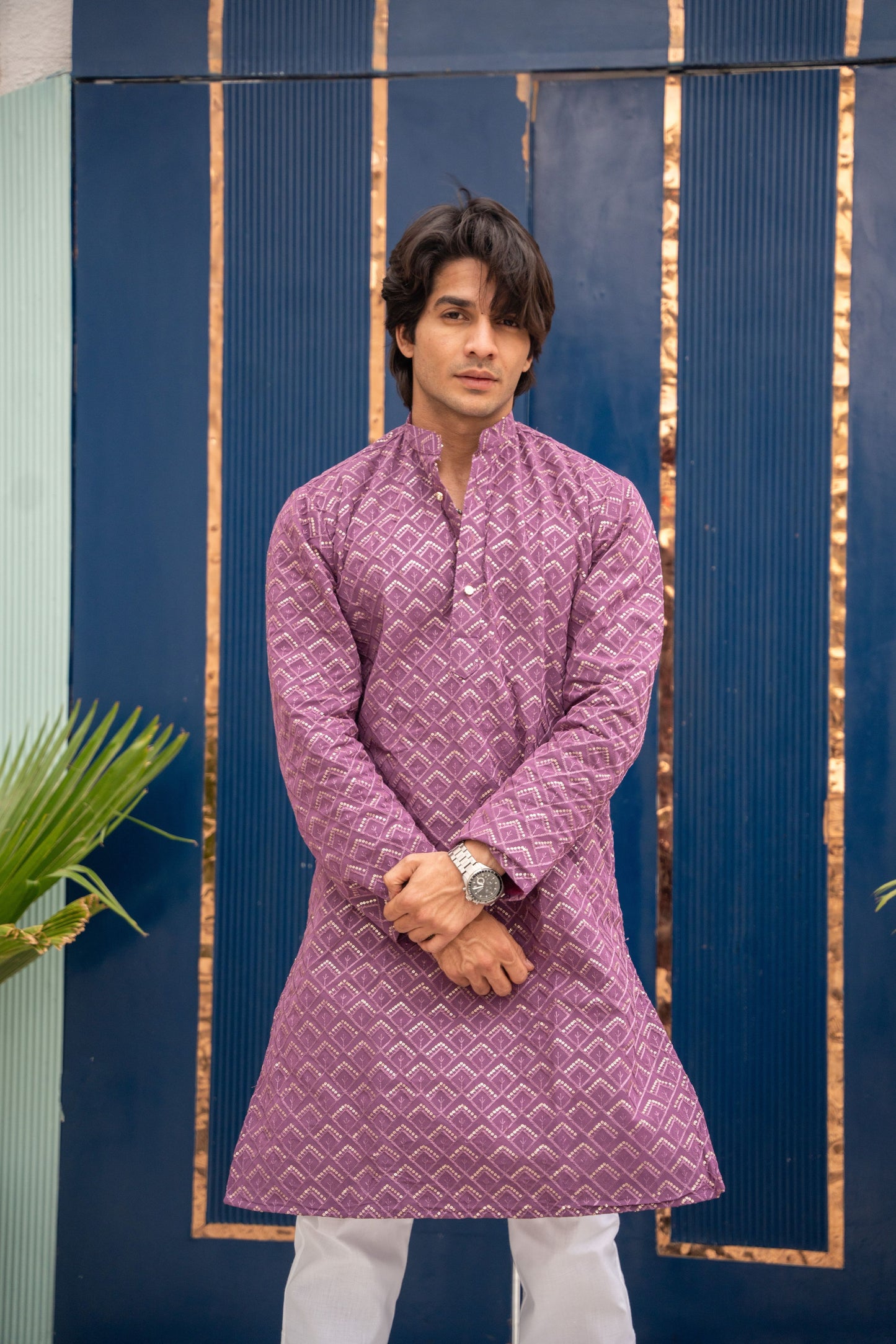 A man wearing a purple kurta paired with white pants, standing confidently with a relaxed expression.