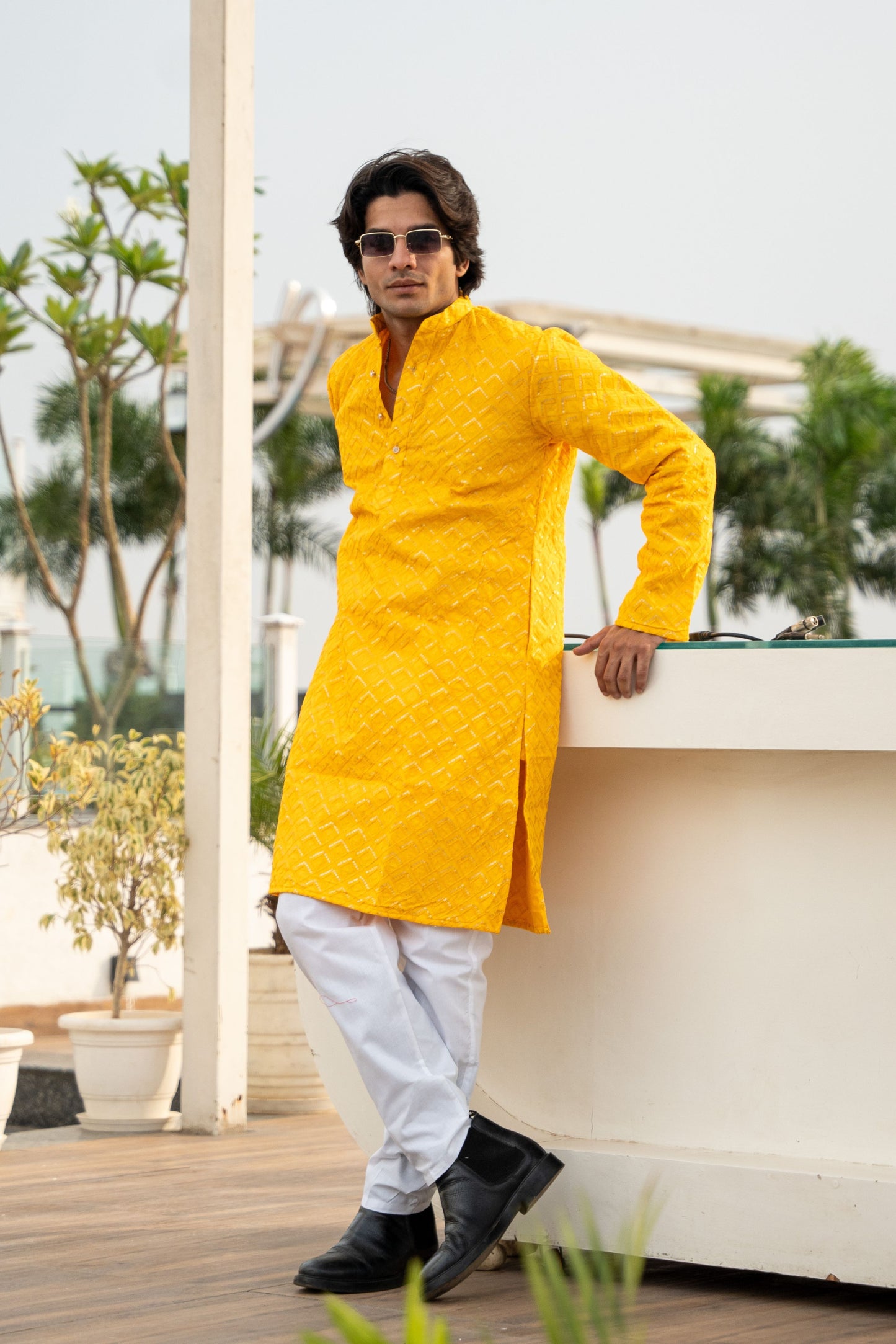 A man wearing a bright yellow kurta paired with white pants, standing confidently with a smile.