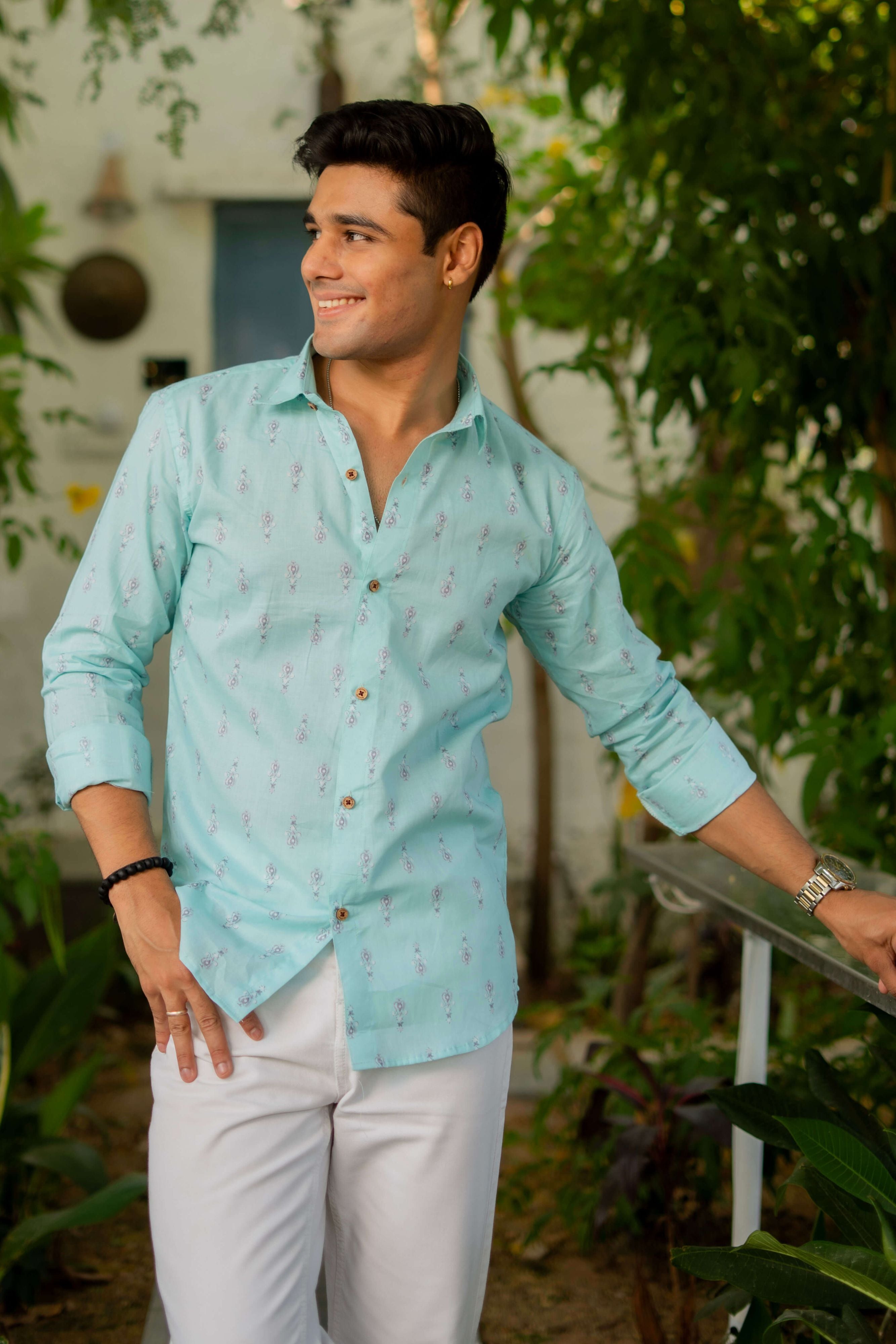 Man buttoning a light green shirt with paisley motifs outdoors.