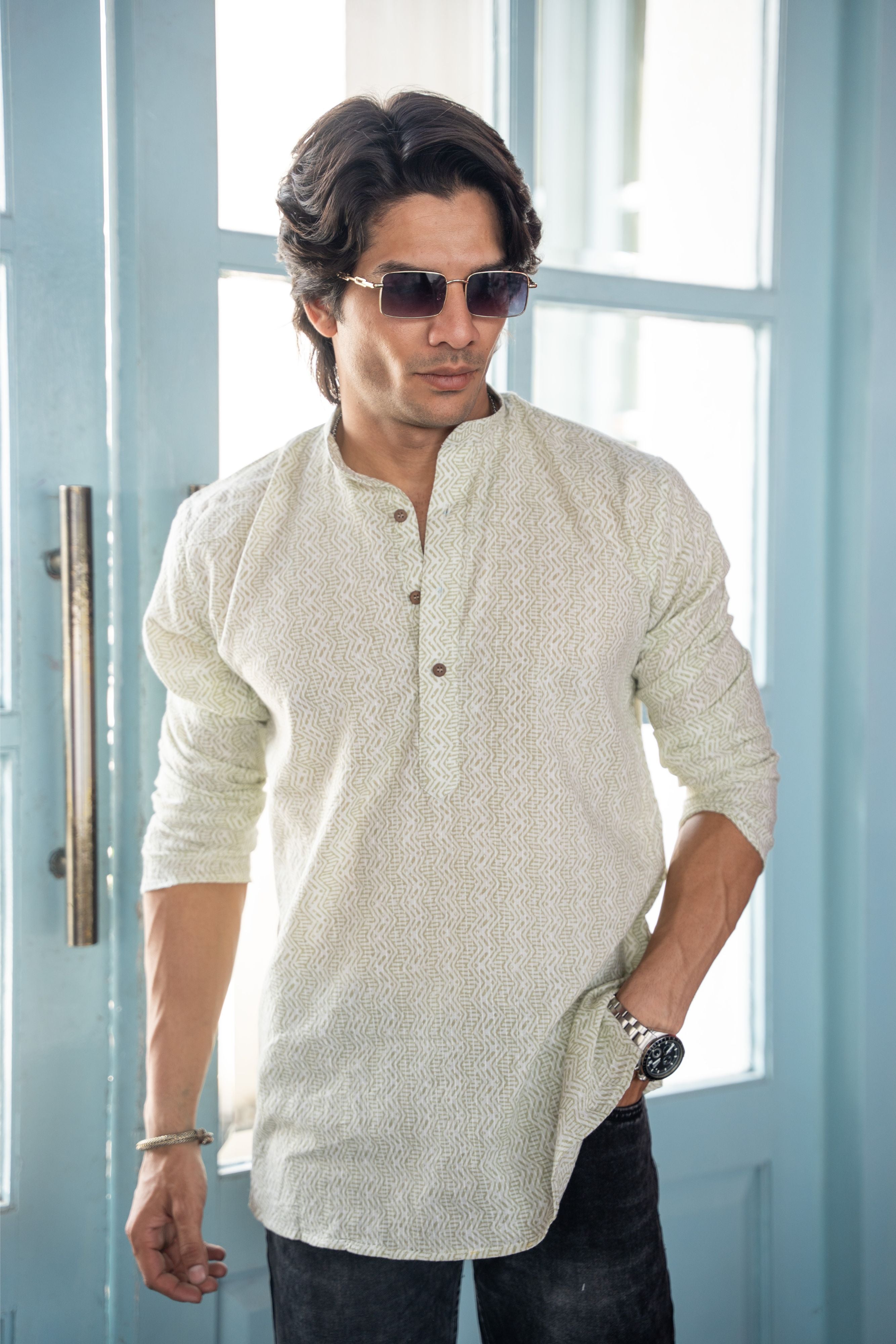 Indian man wearing a white color short kurta with pastel green tribal print. standing in front of a blue gate