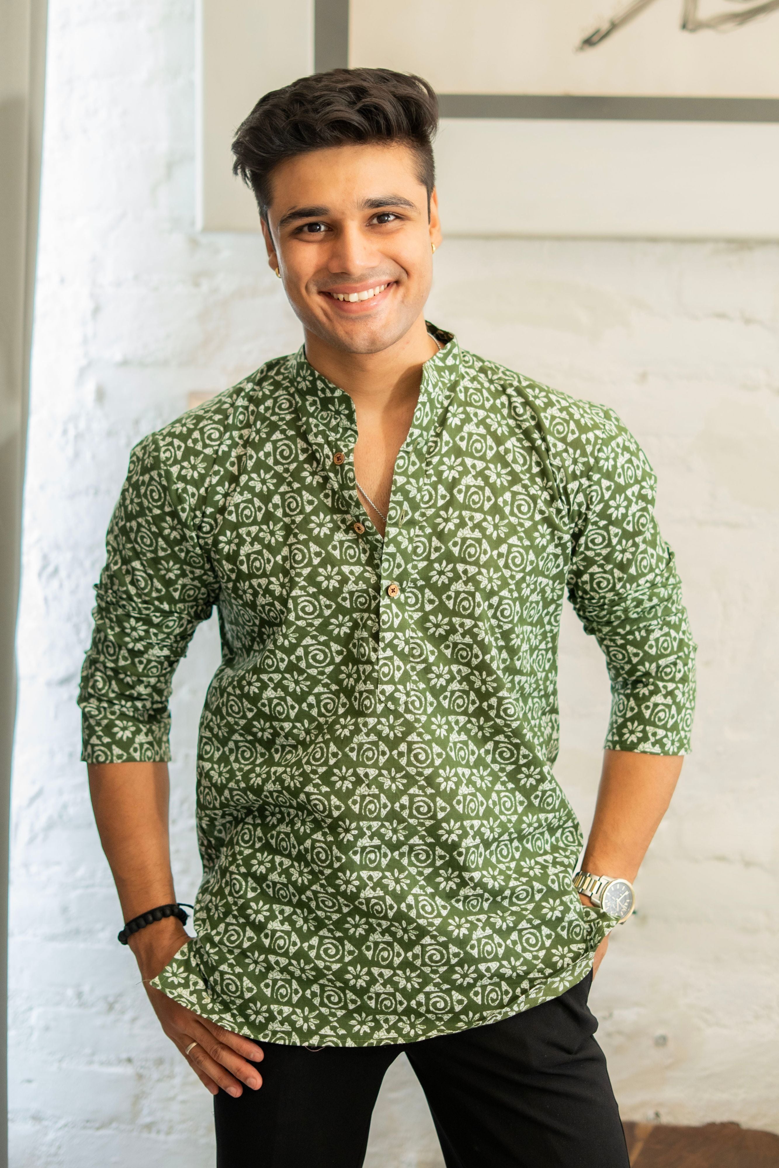 A person wearing a pistachio green short kurta with tribal print, paired with white pants. Standing in front of a white wall. 