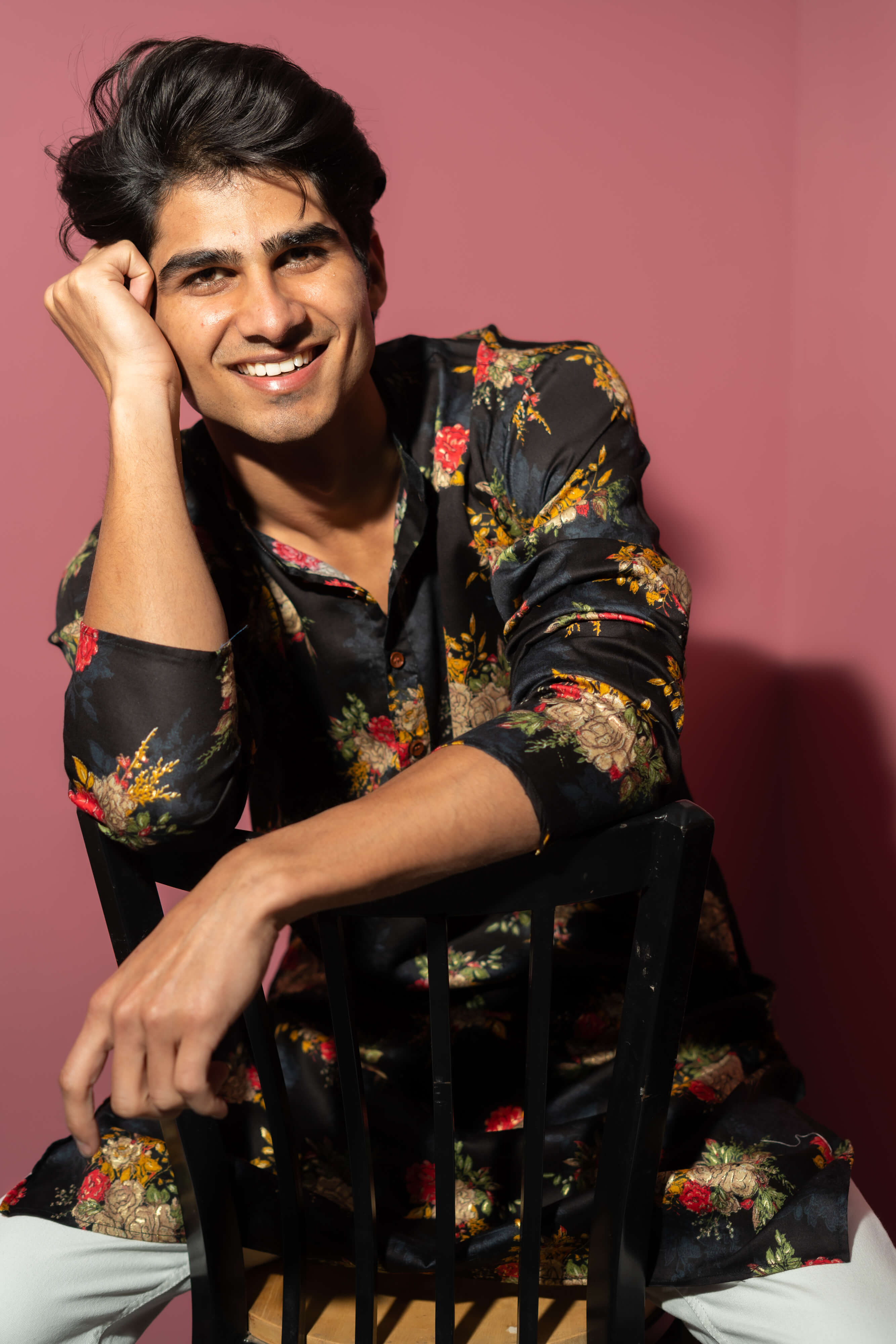 A young man in a black kurta sit ting on a chair, smiling warmly at the camera.
