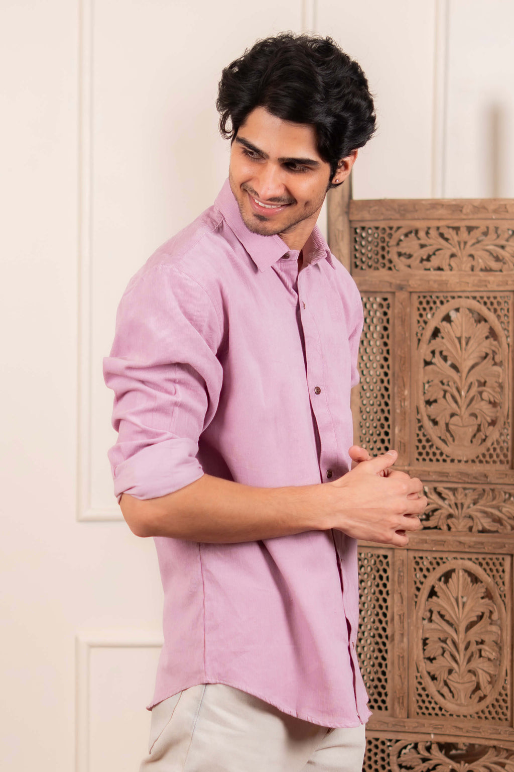 Man wearing a pink shirt standing next to a wooden carved piece.