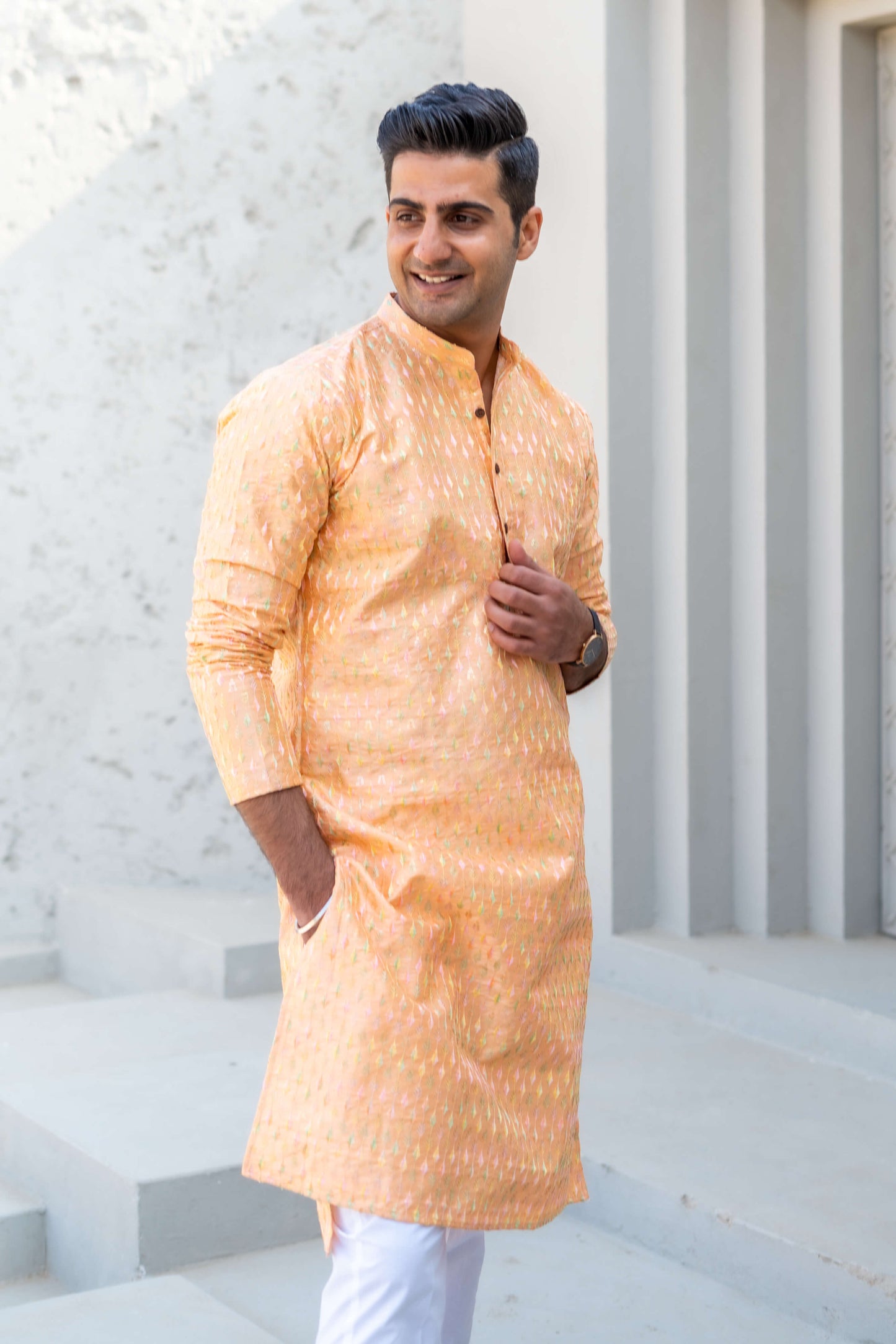 an Indian man wearing saffrin color long kurta with white jeans