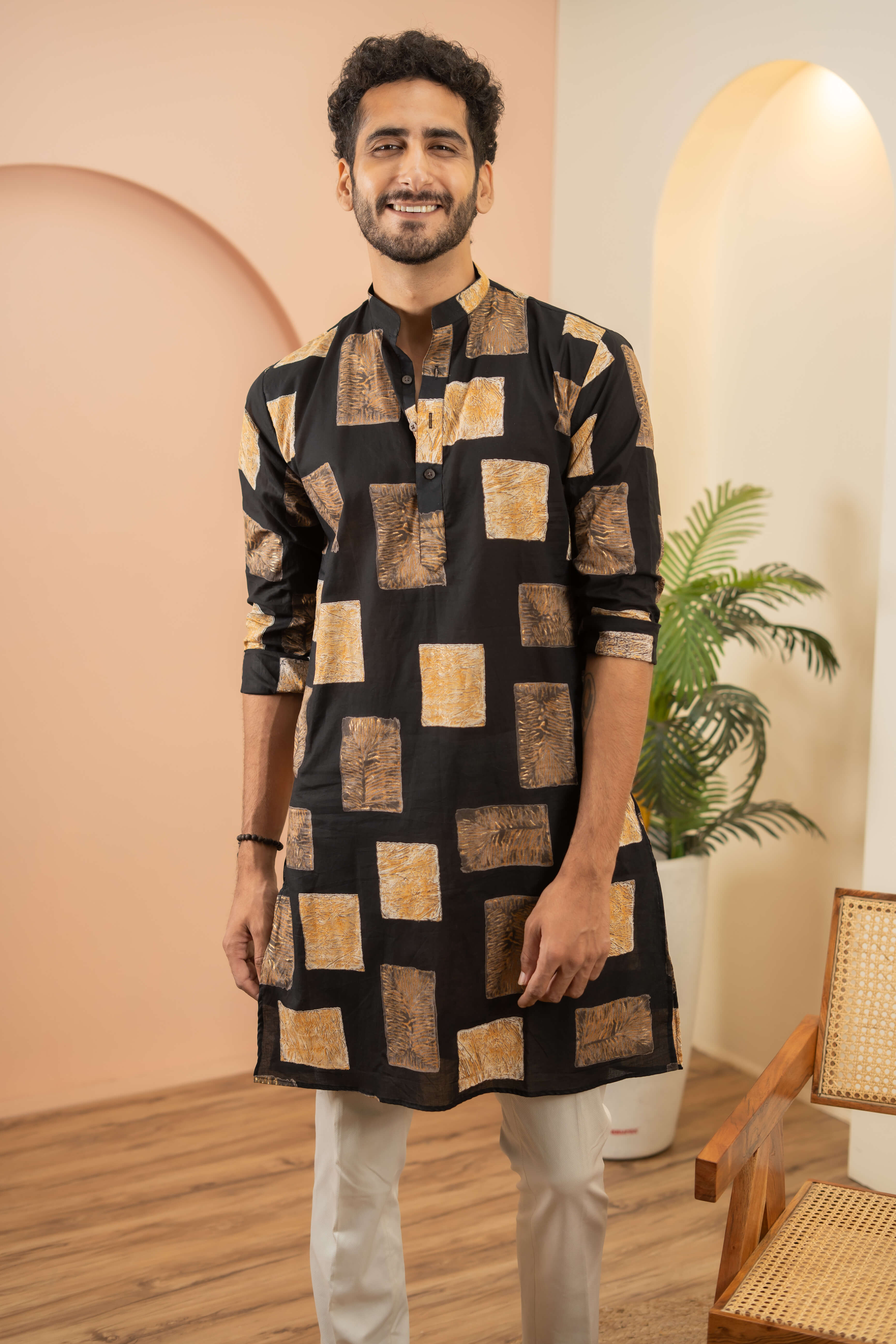 A person wearing a black kurta with a pattern of large, irregularly shaped squares in shades of brown and beige.