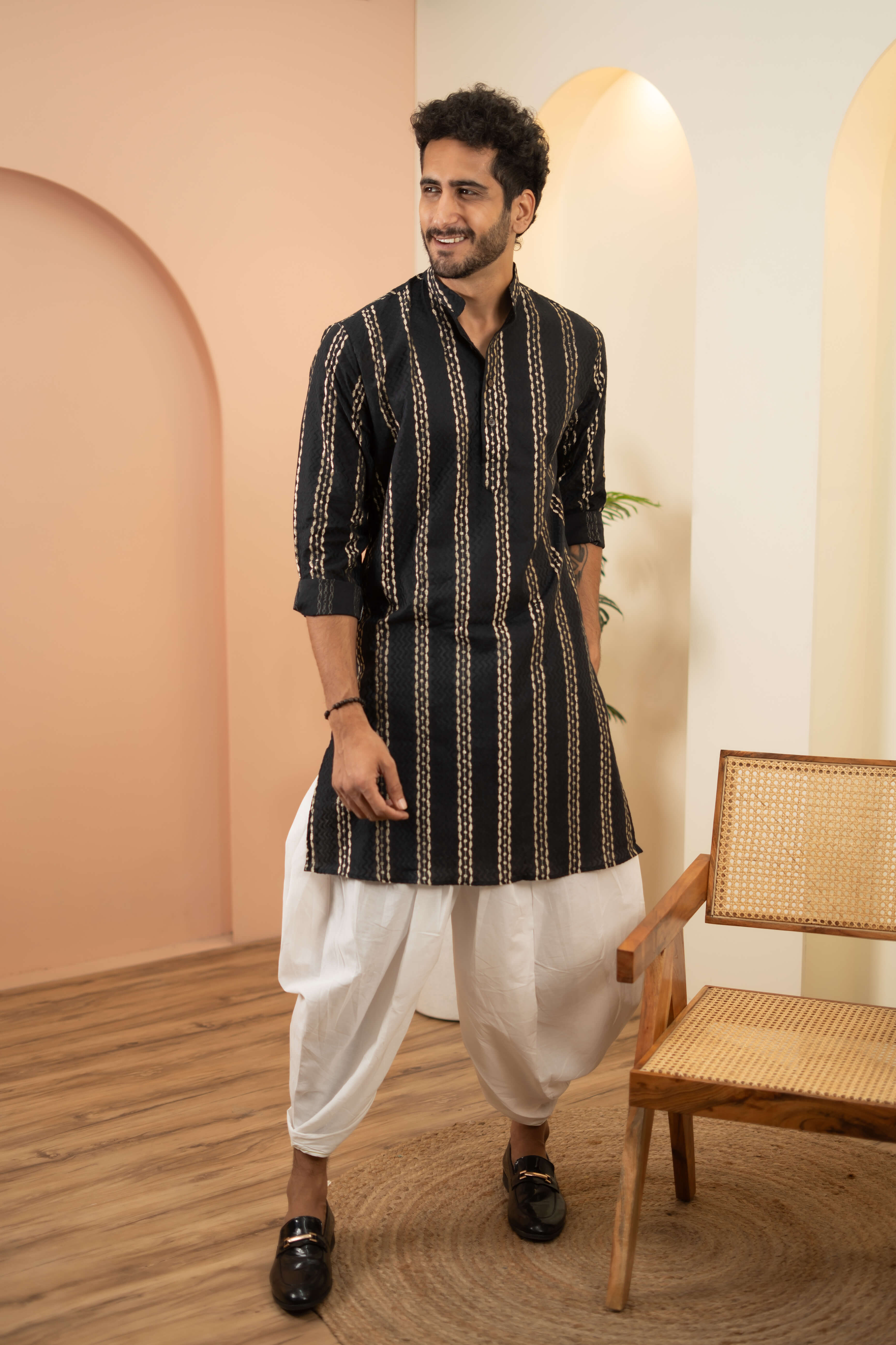 An indian man wearing a black zari work kurta. featuring a doti and black shoes. 