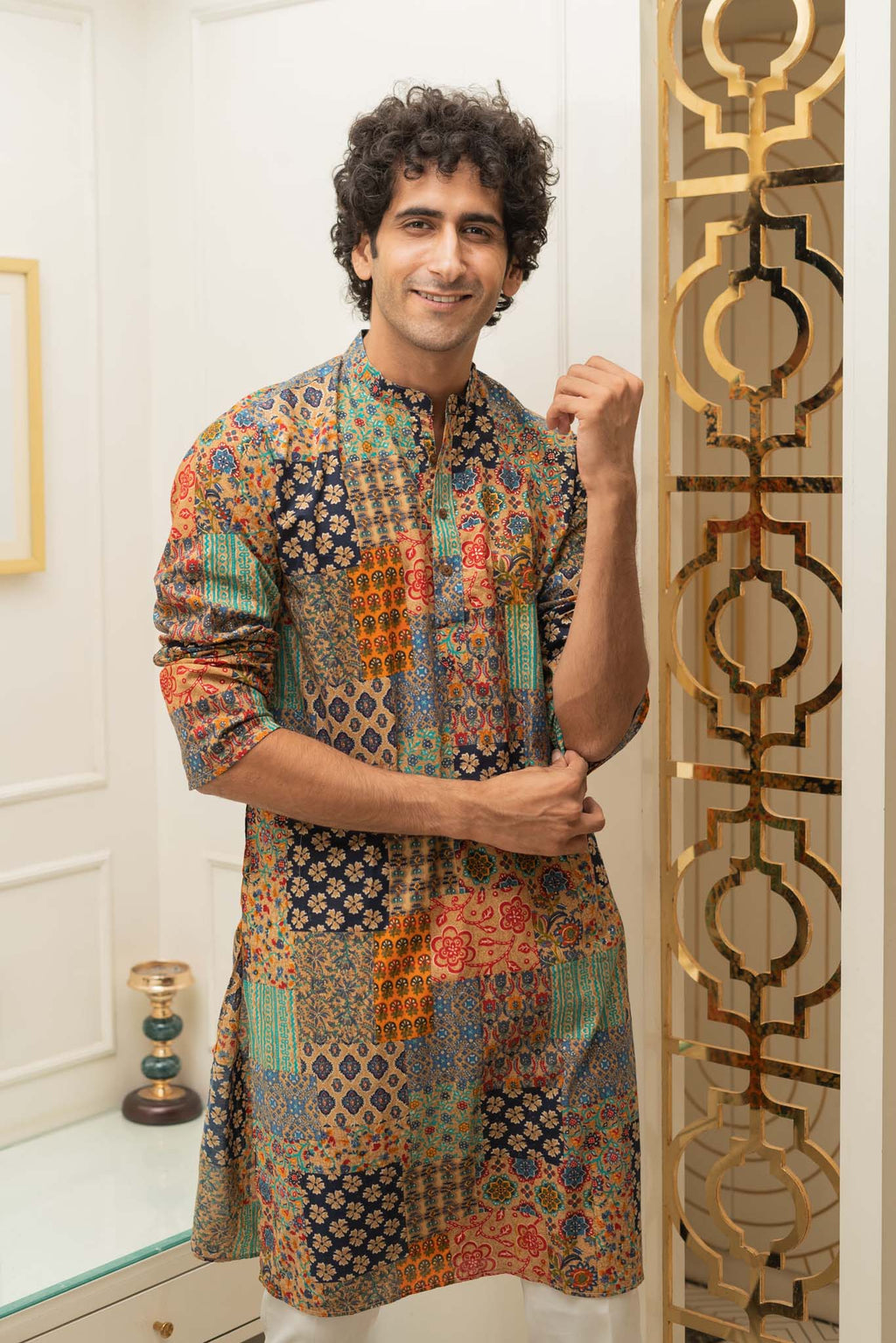 Man wearing a colorful patterned kurta standing in a room with decorative elements.