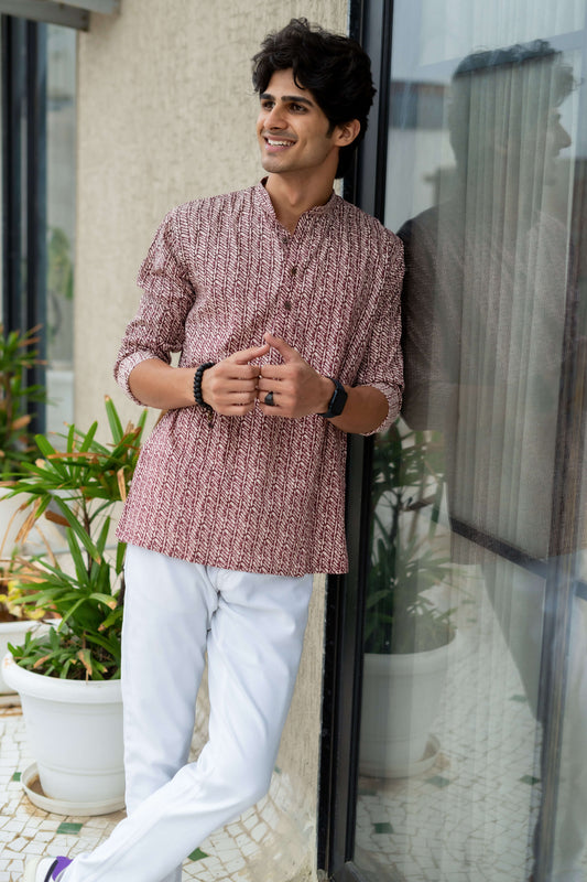 An Indian man wearing a dark wine color short kurta with a white pant. 